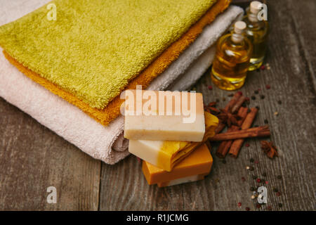 close-up shot of soap pieces with stacked towels, spices and massage oil on rustic wooden tabletop Stock Photo