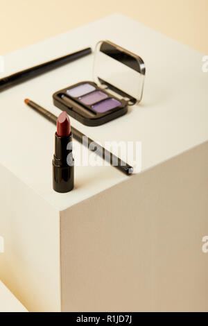 close-up shot of lipstick with purple eyeshadows case and brushes on beige Stock Photo