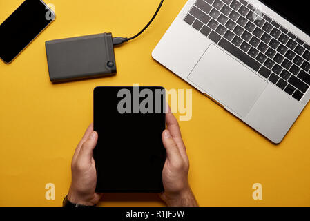 cropped shot of man using tablet on yellow surface with laptop and portable hdd Stock Photo