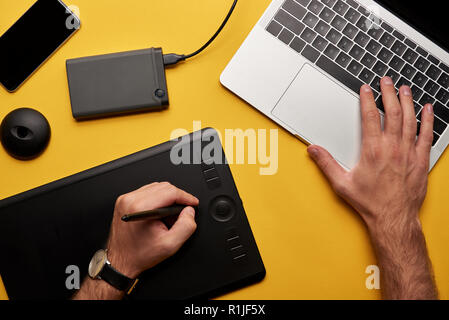 cropped shot of graphics designer working with laptop and graphics tablet on yellow surface Stock Photo