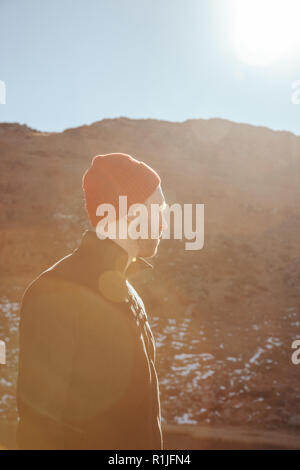 handsome young man in red hat looking away in front of mountain on sunny day, Carpathians, Ukraine Stock Photo