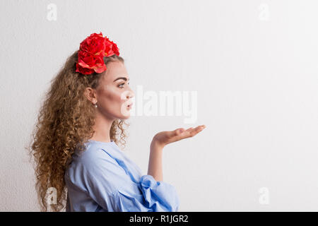 A side view of young beautiful woman with flower headband sending a kiss in studio. Stock Photo