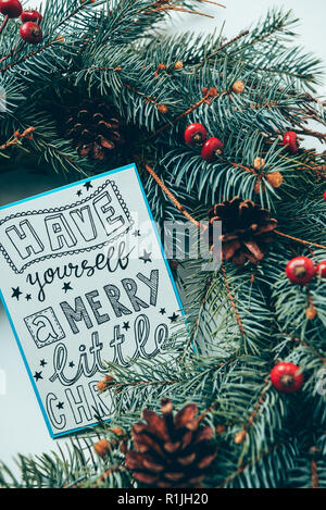 top view of pine tree branches and winter postcard with have yourself merry little christmas lettering on white tabletop Stock Photo