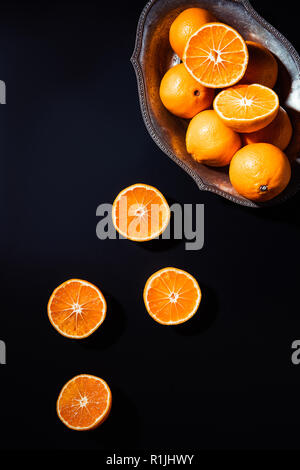flat lay with mandarins and metal bowl on black backdrop Stock Photo