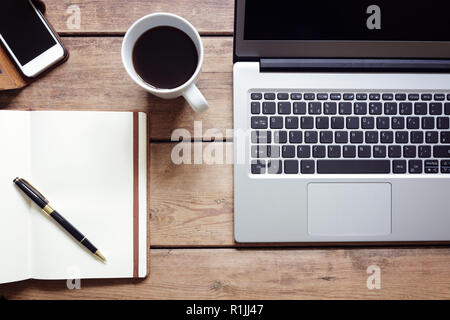 Open laptop with notepad and smartphone workspace on desk from above Stock Photo