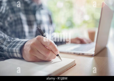 Businessman writing at his desk in office with a laptop computer Stock Photo
