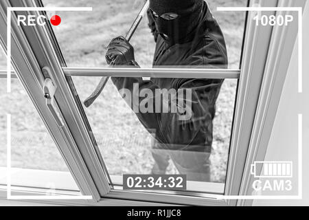 CCTV view of burglar breaking in to home through window with crowbar Stock Photo