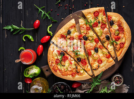 Delicious seafood shrimps and mussels pizza on a black wooden table. Italian food. Top view Stock Photo