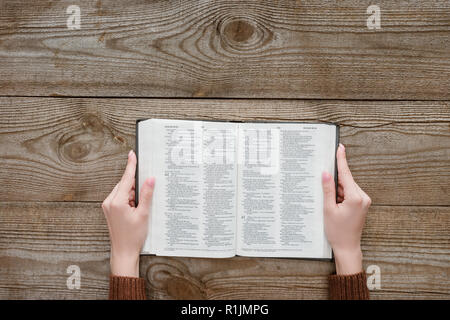 cropped shot of woman holding opened holy bible on wooden surface Stock Photo