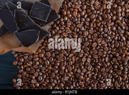 Roasted fragrant beans of black coffee are scattered on a black wooden table, on which black chocolate is lying Stock Photo