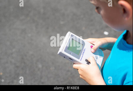 Young boy using his nintendo gameboy to play computer games. Nineties setting. outdoors setting. Stock Photo
