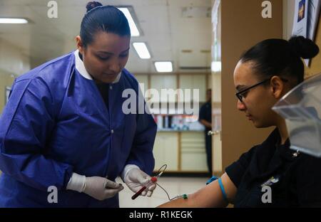 ATLANTIC OCEAN (Oct.15, 2018) – Hospital Corpsman 2nd Class Nancy Torres, from Fresno, Calif., assigned to the laboratory, takes a  blood sample from Hospital Corpsman 3rd Class Vanessa Johnson, from Los Angeles, aboard the hospital ship USNS Comfort (T-AH 20). Comfort is on an 11-week medical support mission to Central and South America as part of U.S. Southern Command’s Enduring Promise initiative. Working with health and government partners in Ecuador, Peru, Colombia and Honduras, the embarked medical team will provide care on board and at land-based medical sites, helping to relieve pressu Stock Photo
