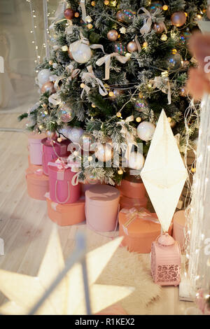 Pink boxes with gifts under the artificial pale green tree.Cozy home atmosphere of the festival Stock Photo