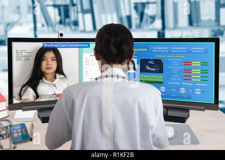 Female doctor working with two computers for distance patient consultation and searching her health information from medical record system. Stock Photo