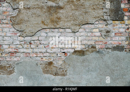 Old and weathered grungy broken brick wall from abandoned house partly covered with old cement with peeling paint coating as texture background. Stock Photo