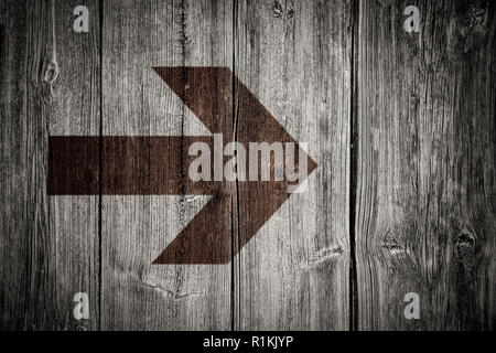 Brown burned wood arrow over old grungy and weathered white and grey painted wooden wall plank texture background with vignetting add dark corners wit Stock Photo