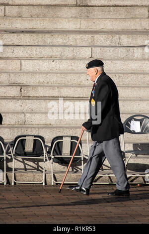 An Elderly British war veteran wearing his medals and beret using his walking stick walking to take his place for a remembrance day parade Stock Photo