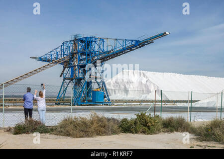 Spain salt works in Santa Pola. Heap of sea salt and industrial machine, Alicante province, Couple rear view People taking photos Costa Blanca Spain Stock Photo