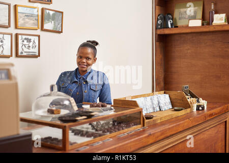 Artisanal chocolate shop owner smiling while standing behind her counter Stock Photo