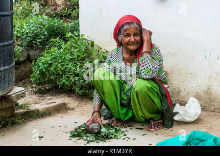An elderly woman grinds the herbs on the concrete floor with a stone pestle. India Himachal Pradesh June 2018 Stock Photo
