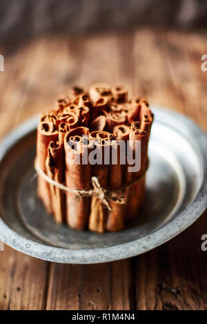 Bunch of Cinnamon sticks on a metallic rustic plate over a wooden table. Stock Photo
