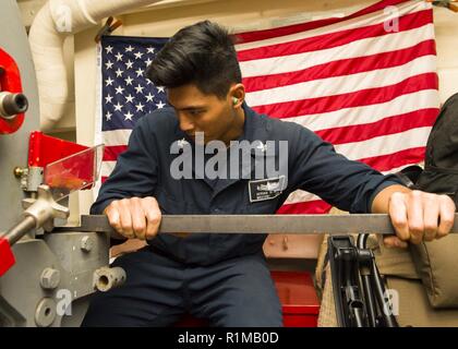 MEDITERRANEAN SEA (Oct. 22, 2018) Machinery Repairman 2nd Class Adrian Albo aligns metal in preparation for using a punching and shearing machine aboard the San Antonio-class amphibious transport dock ship USS Anchorage (LPD 23) in the Mediterranean Sea, Oct. 22, 2018. Anchorage and embarked 13th Marine Expeditionary Unit are deployed to the U.S. 6th Fleet area of operations as a crisis response force in support of regional partners as well as to promote U.S. national security interests in Europe and Africa. Stock Photo