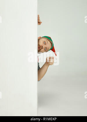 The happy smiling friendly man dressed like a funny gnome or elf pointing to camera on an isolated gray studio background. The winter, holiday, christmas concept Stock Photo