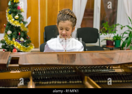 A girl in a beautiful dress plays on a brown grand piano Stock Photo