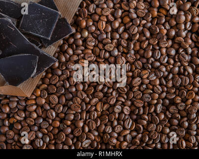 Roasted fragrant beans of black coffee are scattered on a black wooden table, on which black chocolate is lying Stock Photo
