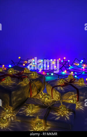 Christmas gift boxes on blue background. Burlap canvas and white wrapping paper with red ribbon.  Gold decoration lights. Empty copy space for text. Stock Photo