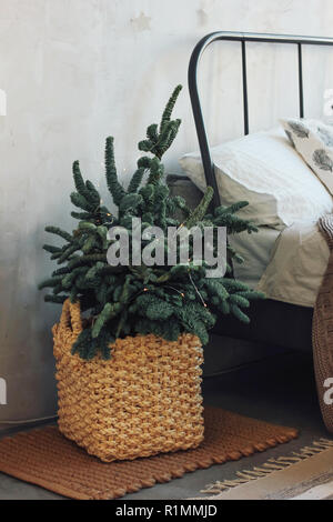 Christmas tree in a wicker basket by the bed. Minimalistic Scandinavian decor Stock Photo