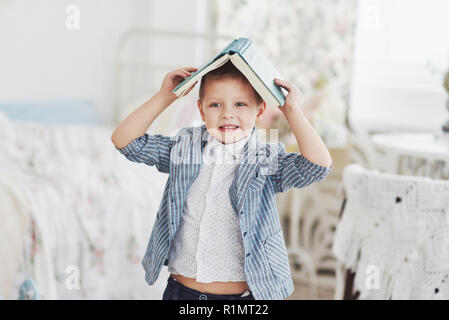 Photo of diligent schoolboy with book on his head doing homework. The schoolboy is tired of doing homework Stock Photo