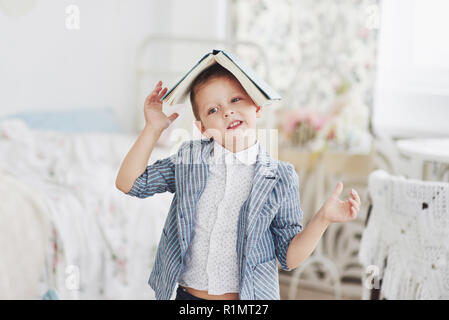 Photo of diligent schoolboy with book on his head doing homework. The schoolboy is tired of doing homework Stock Photo