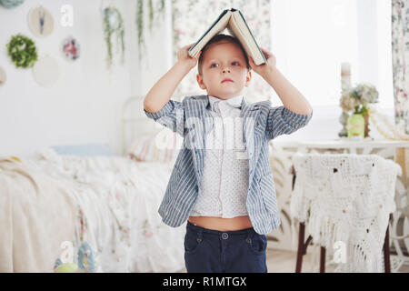 Photo of diligent schoolboy with book on his head doing homework. The schoolboy is tired of doing homework Stock Photo