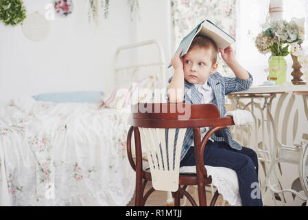 Photo of diligent schoolboy with book on his head doing homework. The schoolboy is tired of doing homework Stock Photo