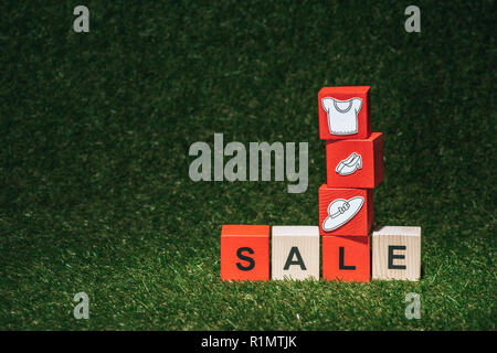 red and wooden alphabet cubes with sale sign and clothes on green grass Stock Photo