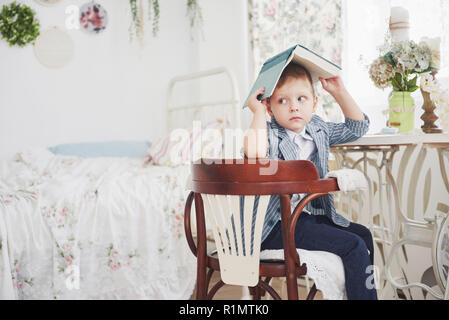 Photo of diligent schoolboy with book on his head doing homework. The schoolboy is tired of doing homework Stock Photo