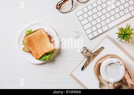 elevated view of paper coffee cup, sandwich and computer keyboard at table in office Stock Photo