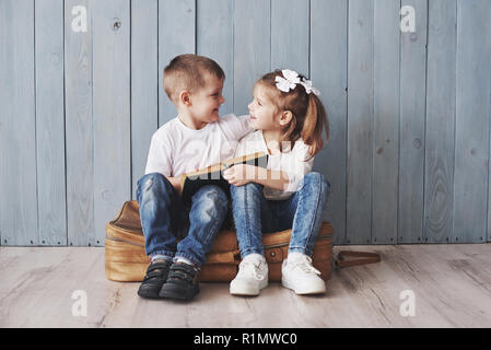 Ready to big travel. Happy little girl and boy reading interesting book carrying a big briefcase and smiling. Travel, freedom and imagination concept Stock Photo