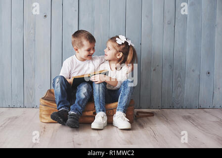 Ready to big travel. Happy little girl and boy reading interesting book carrying a big briefcase and smiling. Travel, freedom and imagination concept Stock Photo