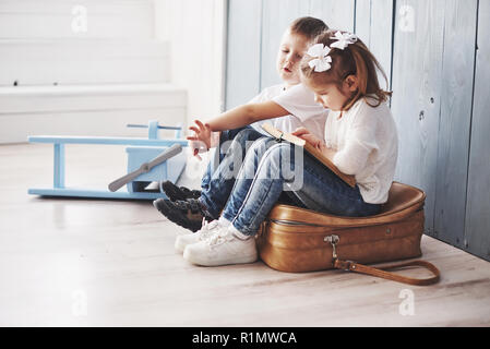 Ready to big travel. Happy little girl and boy reading interesting book carrying a big briefcase and smiling. Travel, freedom and imagination concept Stock Photo