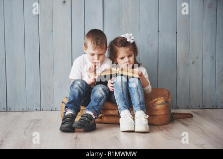 Ready to big travel. Happy little girl and boy reading interesting book carrying a big briefcase and smiling. Travel, freedom and imagination concept Stock Photo