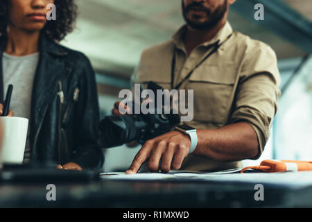 Man holding a digital camera explaining ideas to a model. Photographer pointing at a paper showing it to a model. Stock Photo