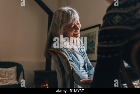 Couple sitting at home talking to each other. Old woman laughing while having a conversation with a person at home. Stock Photo