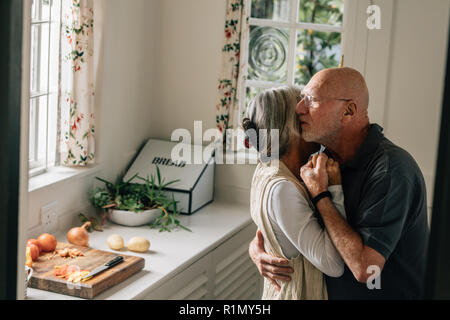 Senior man and woman expressing their love for each other with a warm hug. Elderly couple embracing each other standing in kitchen at home. Stock Photo