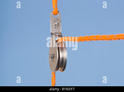 A fixed pulley with an orange rope isolated against a blue background Stock Photo