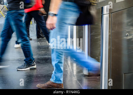 Side view of men passing through stainless steel ticket gates in a public transportation station in Paris, France, with motion blur. Stock Photo