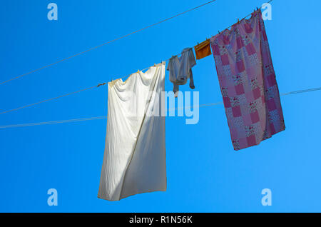 Pajamas and sheets hanging from a thread in front of a saturated blue sky to dry Stock Photo