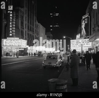 1965, eveningtime and a view along Broadway, mid-town Manhattan, New York City, USA showing the neon lights of the cinemas, theatres, shops and bars in Times Square. The Victory Theatre has the film, 'Who's Minding the Store', featuring comedian Jerry Lewis on the right, while at the New Amsterdam, 'Dracula, Prince of Darkness', was being screened. Opened in 1903, the New Amsterdam Theatre is now the oldest operating theatre on Broadyway, operated by the Disney Company. Stock Photo