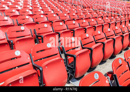 Rows of empty red bleacher seats in a stadium with numbers inside of baseball looking stickers. Stock Photo